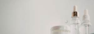 Skincare serums and a cream jar with water droplets around them.