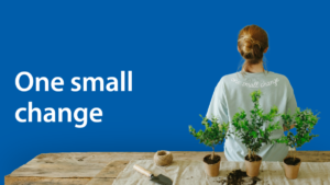 Person viewed from behind standing at a wooden table with small potted plants and gardening tools, with the words ‘One small change’ on a blue background.