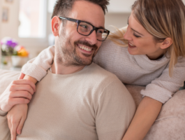 Person sitting on a couch with another person resting an arm on their shoulder, illustrating support during a health or medication conversation.