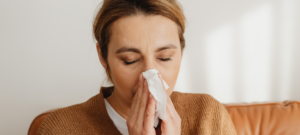 Person sitting indoors holding a tissue near the nose, suggesting nasal congestion or allergy symptoms.